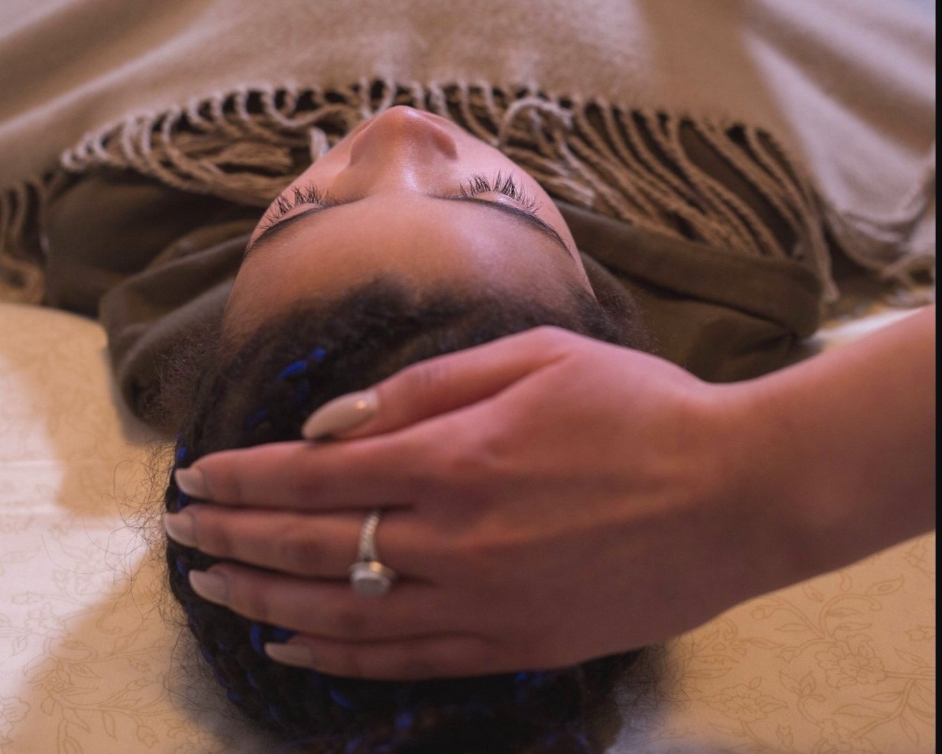 A child is lying down with her eyes closed, receiving a energy healing on her head with practitioners hand gently supporting her scalp.