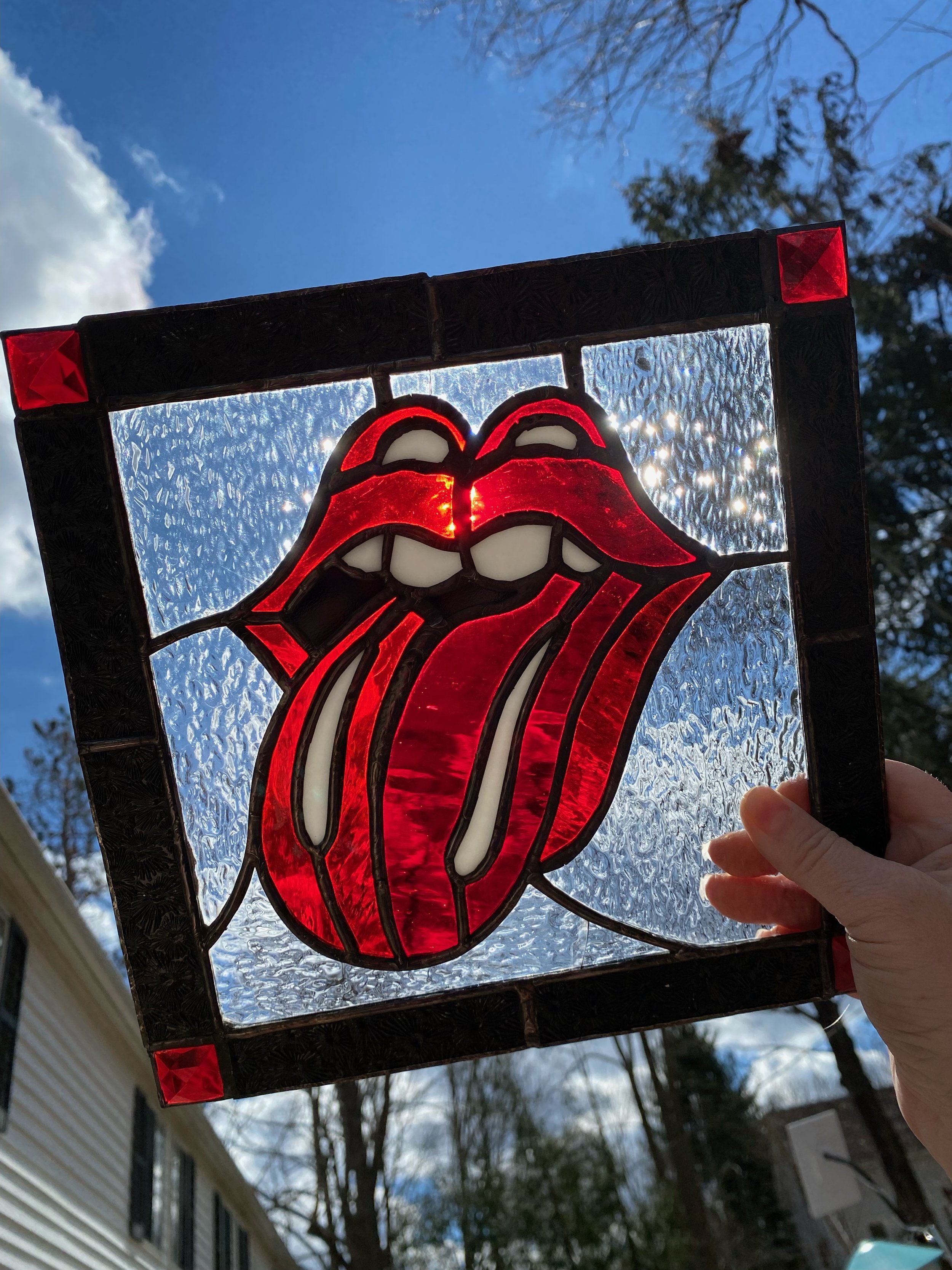 A stained glass window featuring the iconic Rolling Stones 'tongue and lips' logo, held up against the sky.