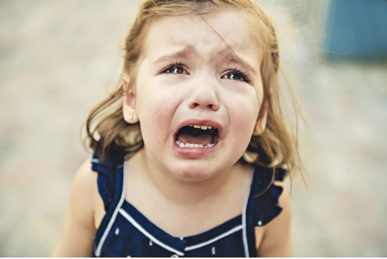 Young girl crying outdoors, wearing a blue dress, close-up.