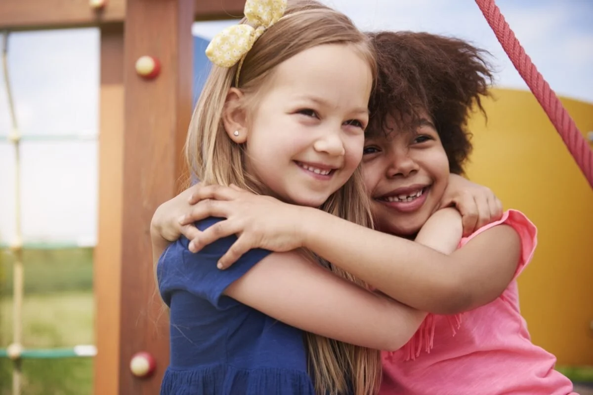 Two young children hugging and smiling at a playground.