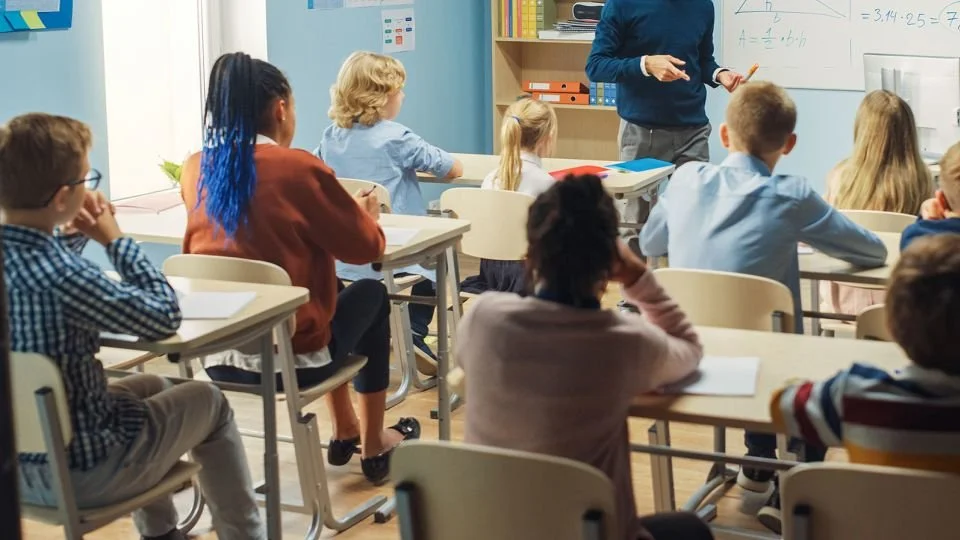 Students sitting in a classroom facing a teacher at a whiteboard.