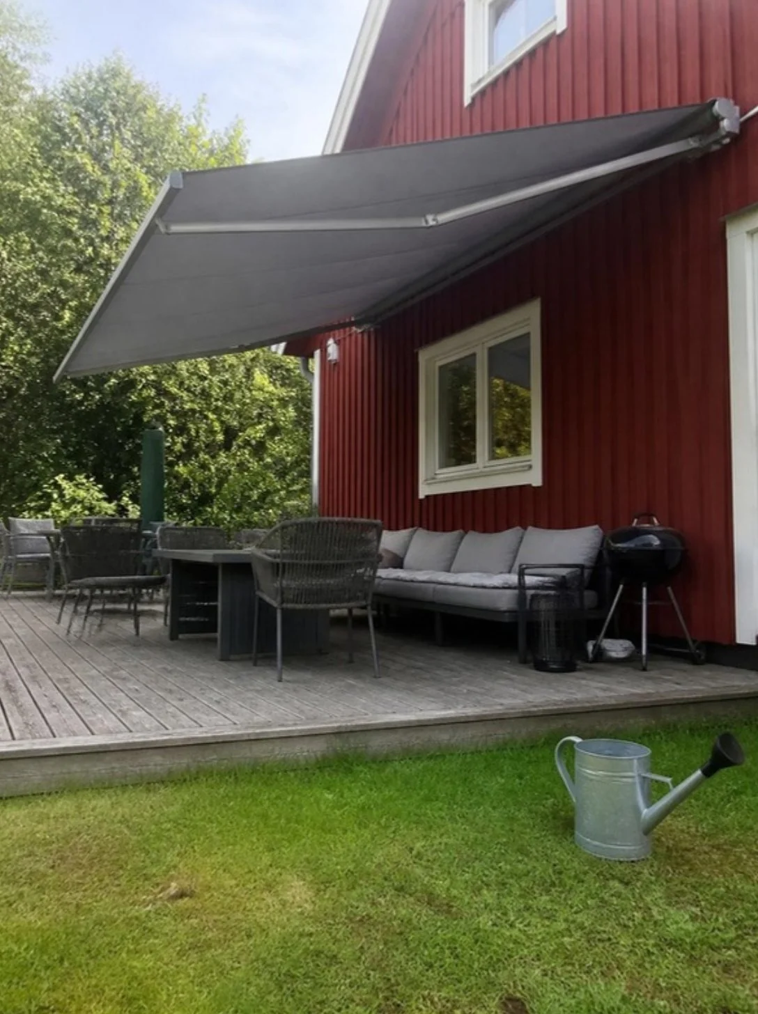 Utfälld grå terrassmarkis över ett trädäck vid ett rött trähus