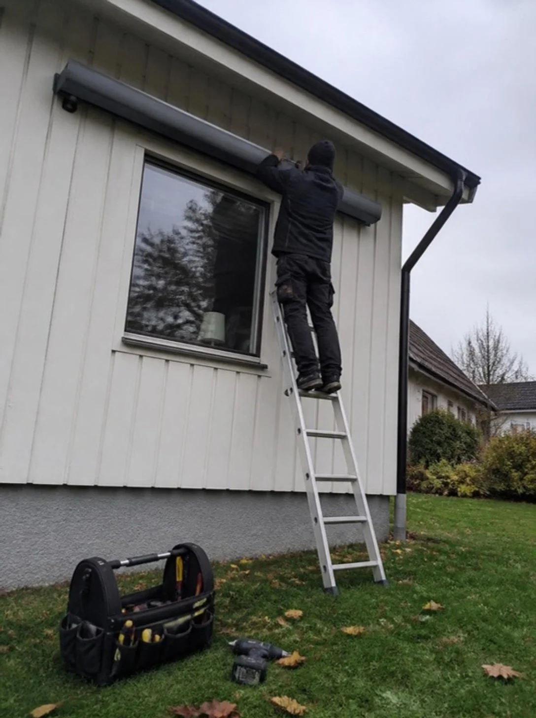 Montör på stege monterar en kassettmarkis på en vit villafasad