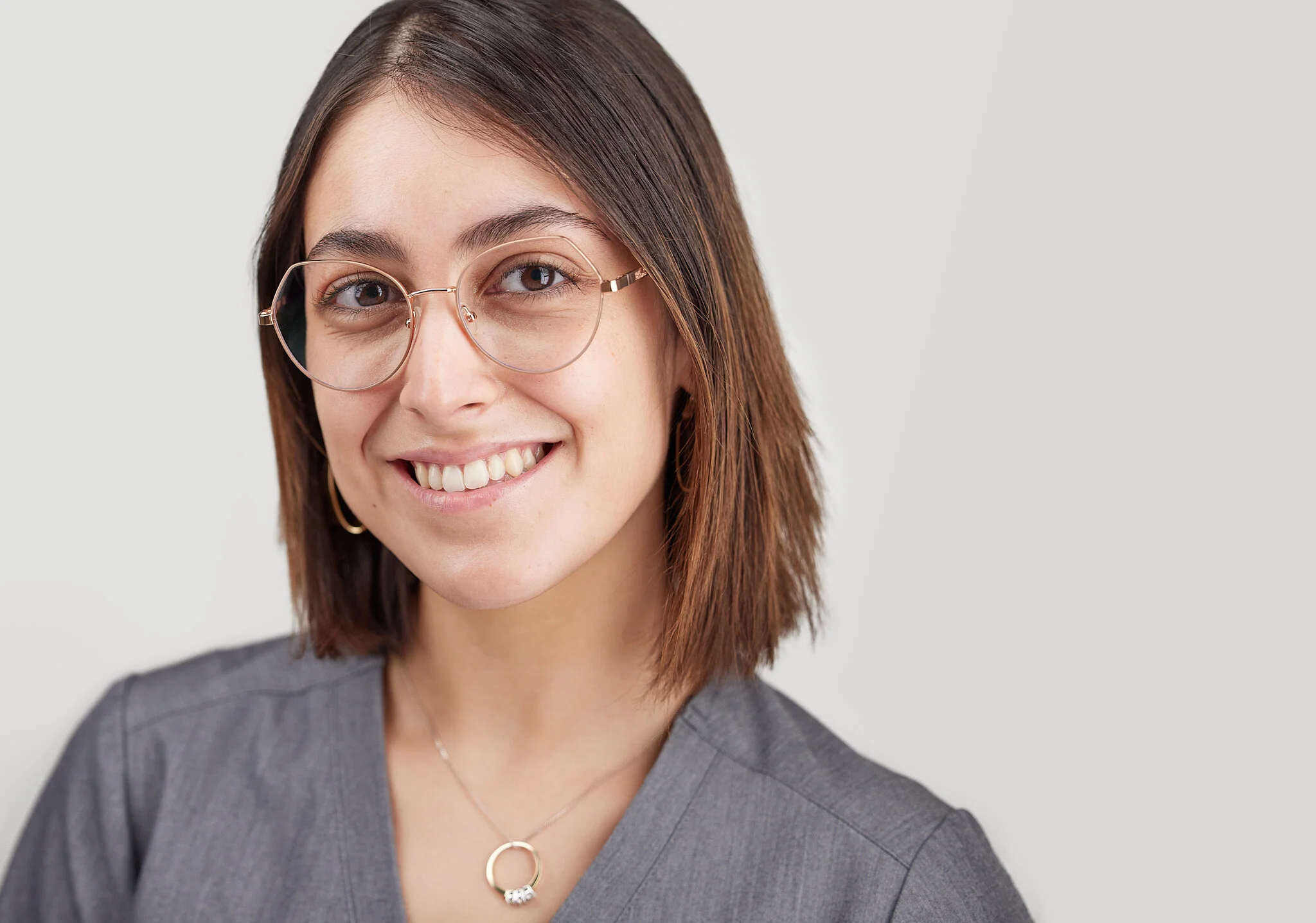 Smiling woman with glasses and brown hair, wearing a gray top and necklace.