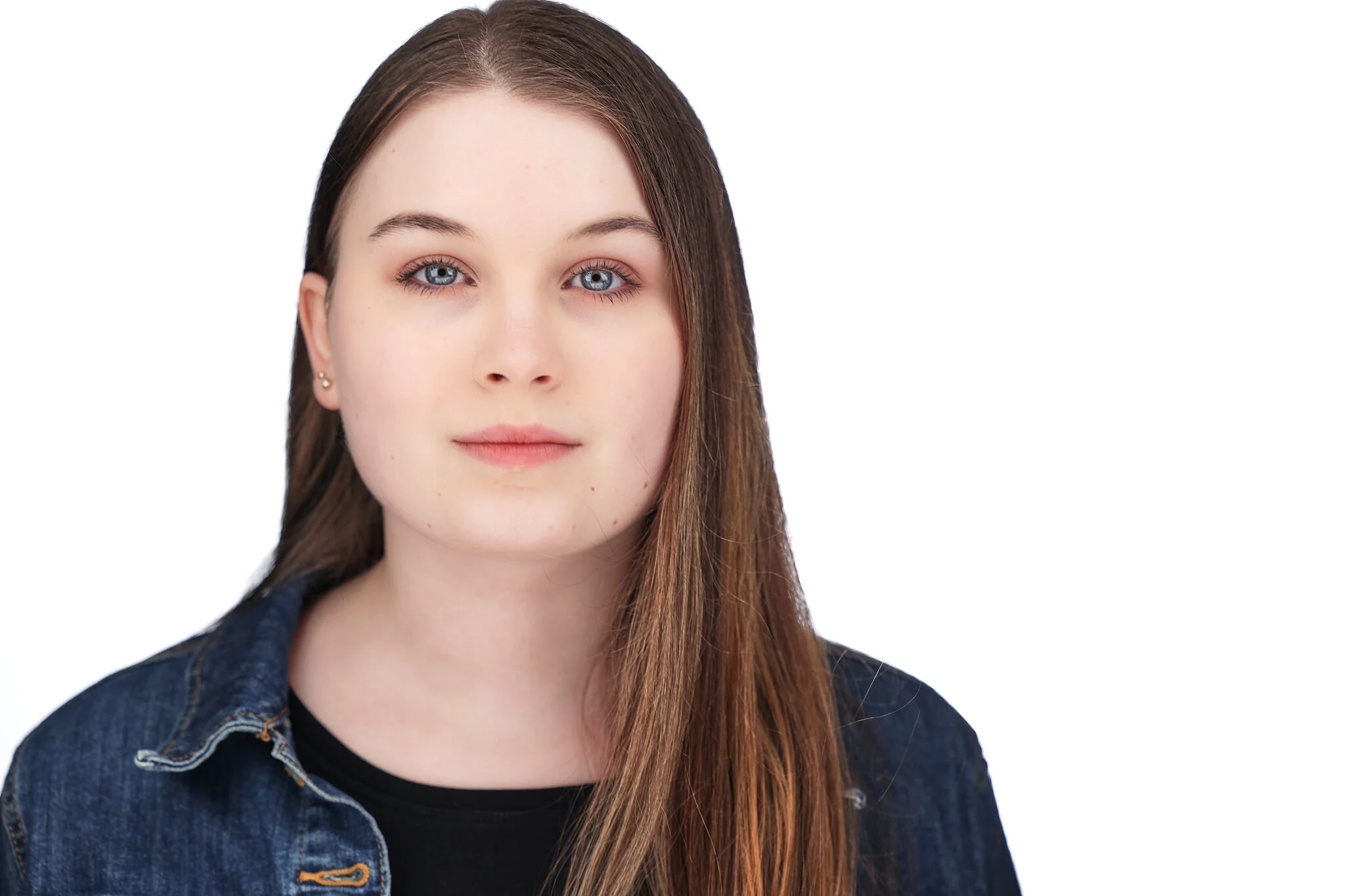 Portrait of a young woman with long hair wearing a denim jacket, facing forward against a white background.