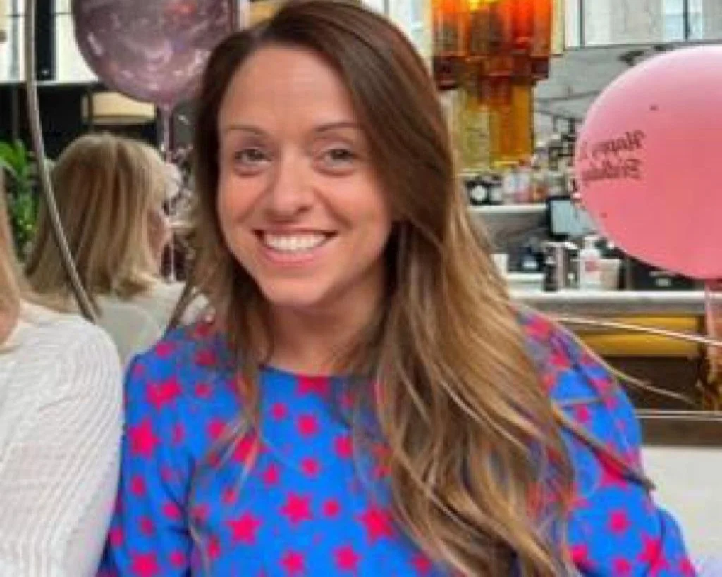 Woman in a blue dress with red stars, smiling in a bar setting with balloons in the background.
