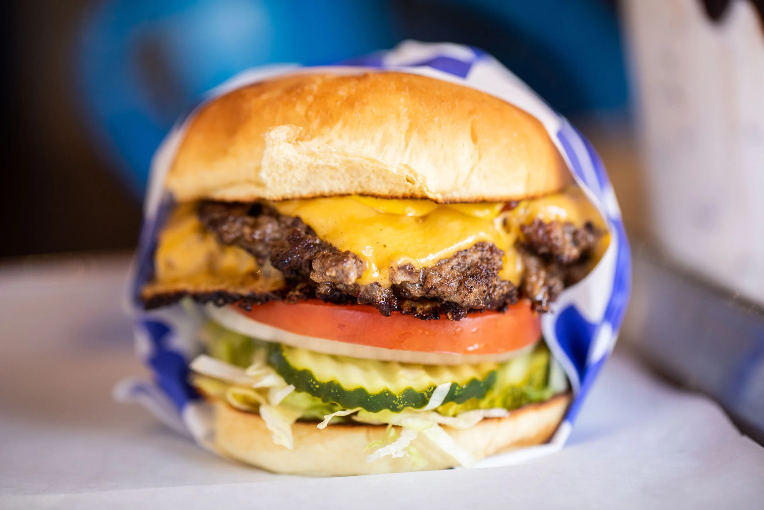 A close-up of a cheeseburger with lettuce, tomato, pickles, beef patty, melted cheese, and a toasted bun.