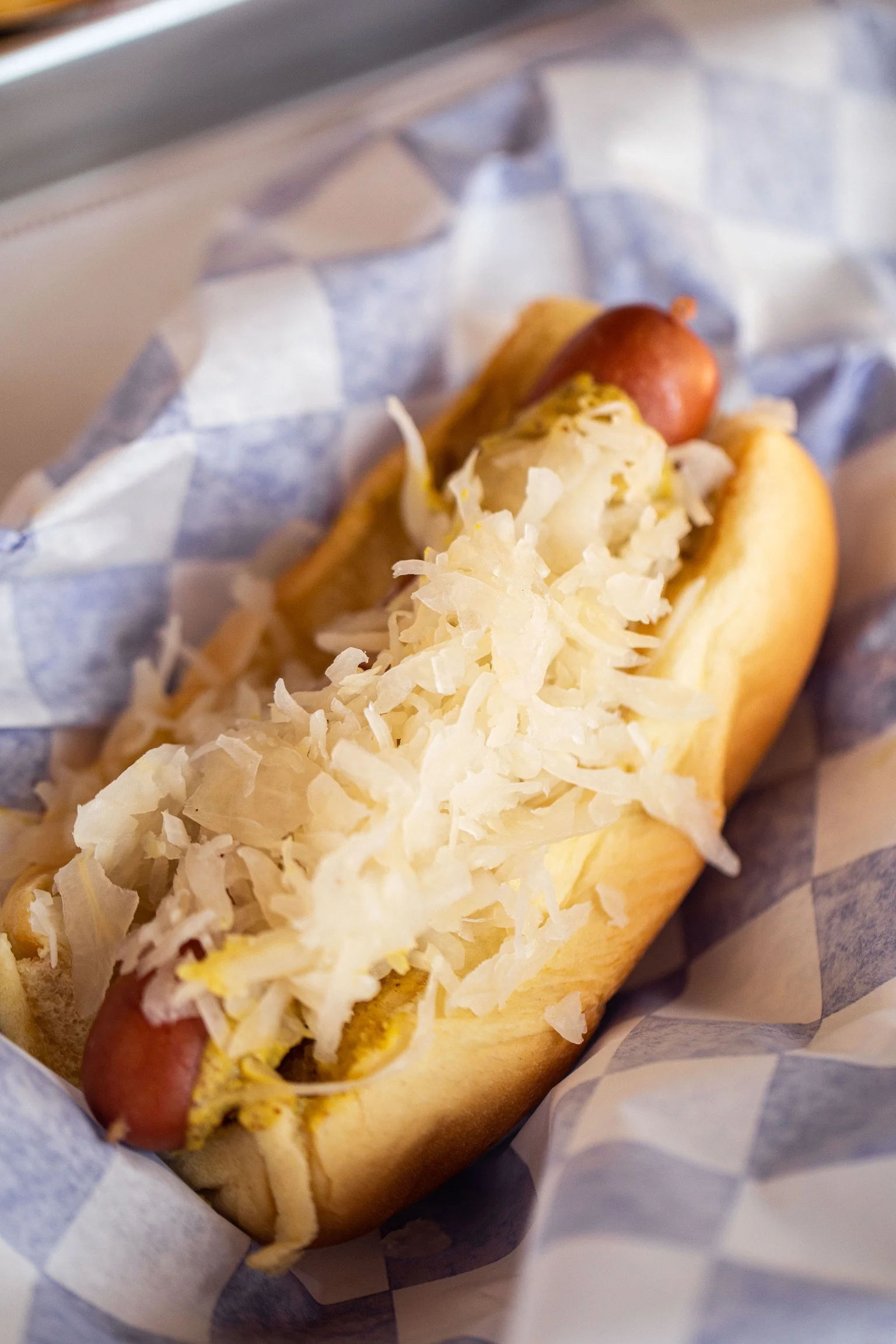 Hot dog topped with shredded cheese in a bun, wrapped in blue and white checkered paper.