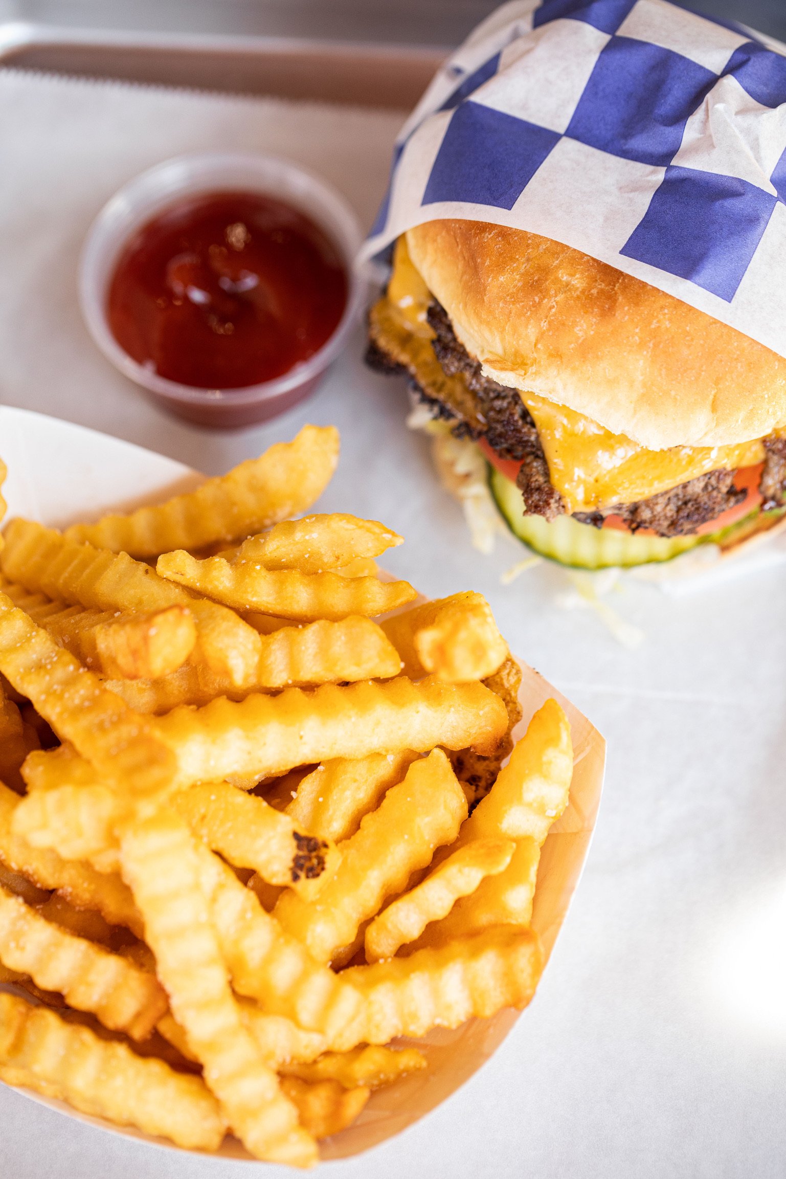 French fries, cheeseburger with lettuce, tomato, cheddar cheese, beef patty, pickles, and sandwich bun, side of ketchup in a cup.