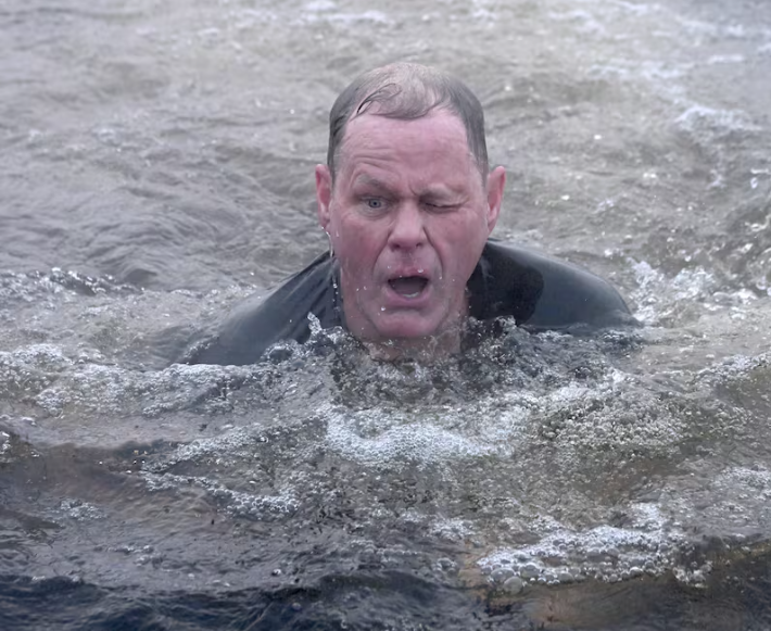 A man in a tuxedo submerged in water up to his shoulders, making an exaggerated facial expression.