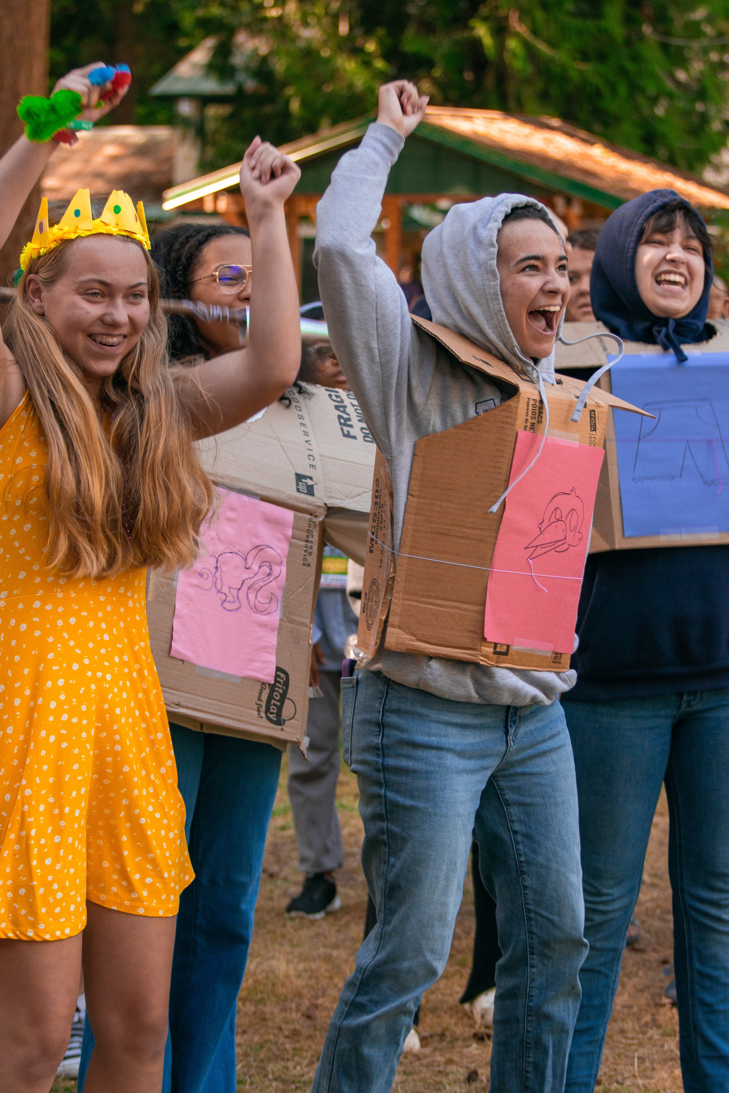 Group of children dressed as dragons and princesses celebrating outdoors, some wearing cardboard costumes and a crown, with smiling faces.