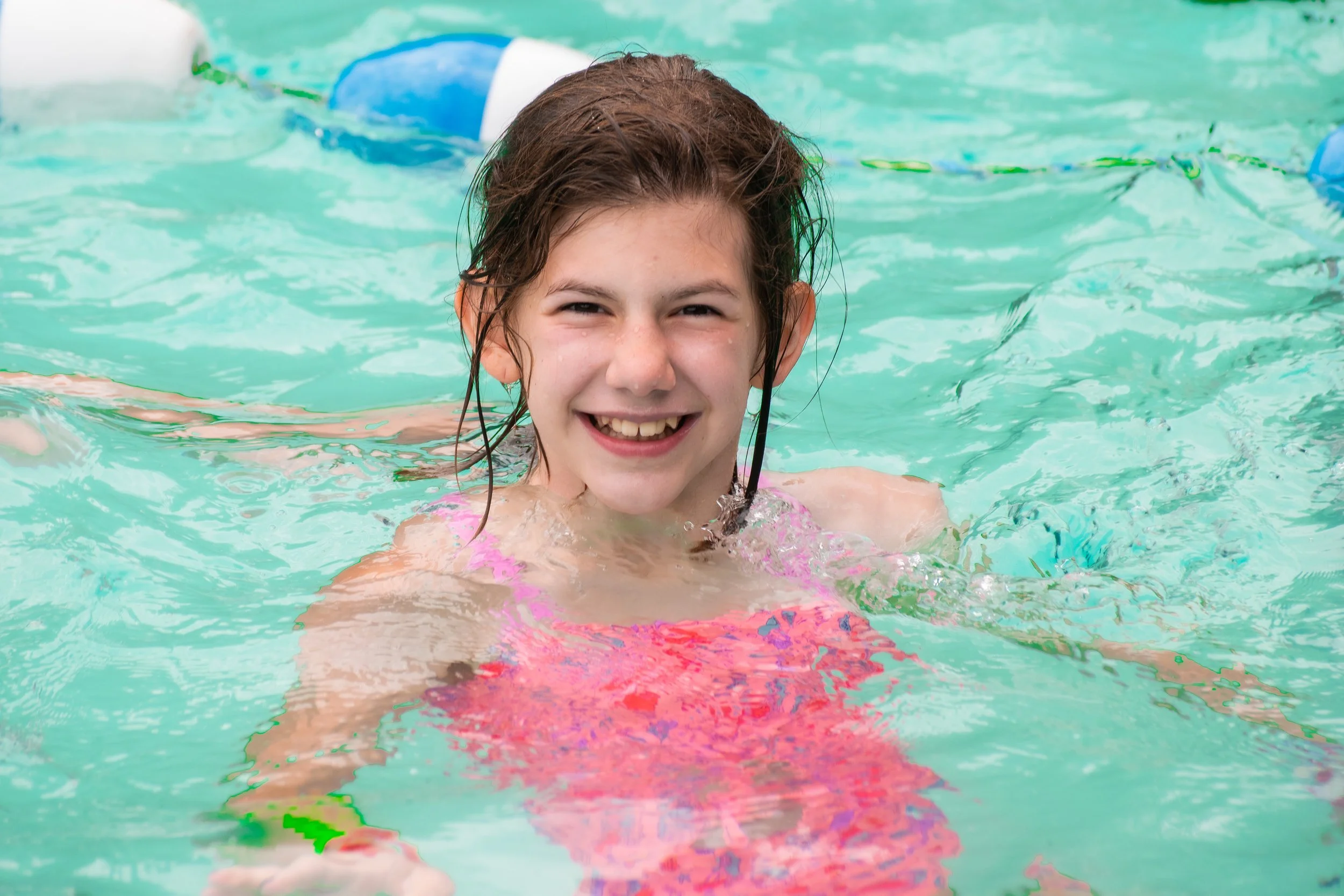 Young girl smiling in a swimming pool with wet hair.