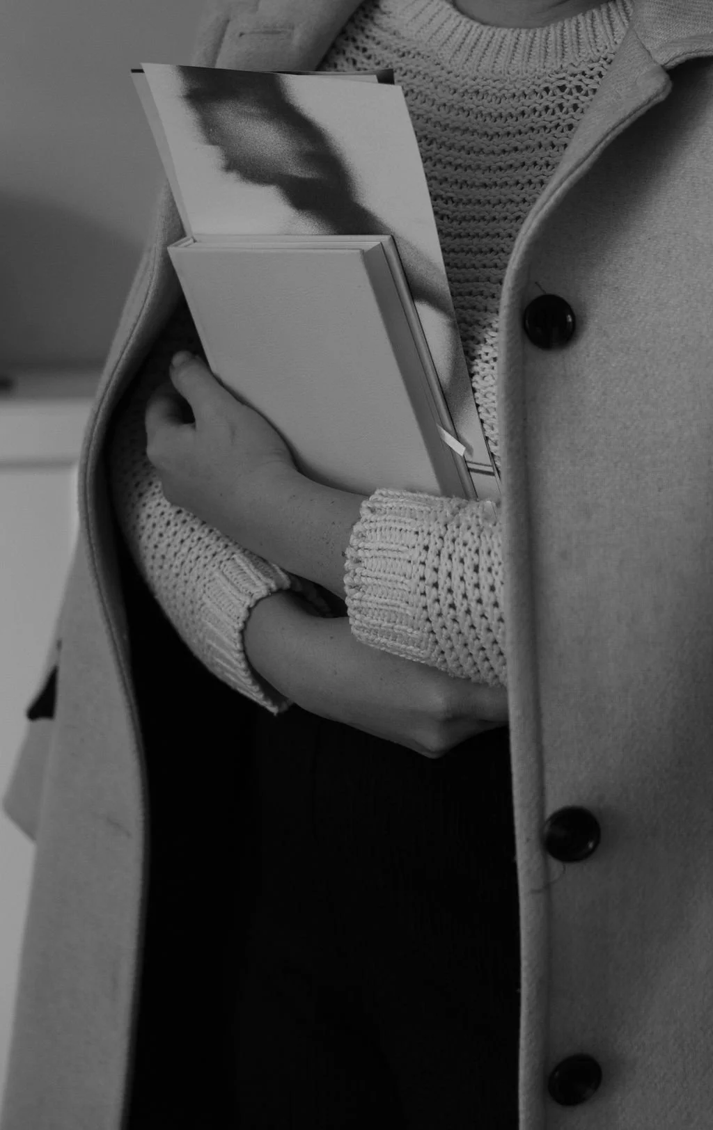 A person in a light-colored coat holding two books or notebooks, one with a black and white abstract cover, wearing a knitted sweater with rolled-up sleeves.Katie McFarlan Dakota Design Company Best Client Process Templates for Interior Designers