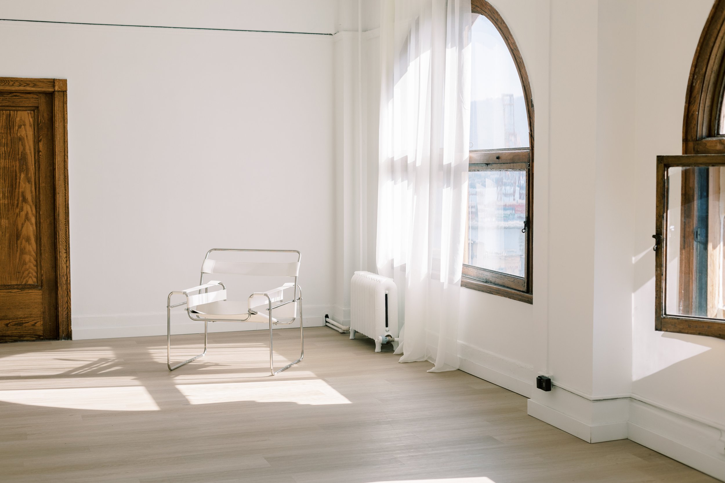 Image of a spacious studio space with clear chair and white window treatments