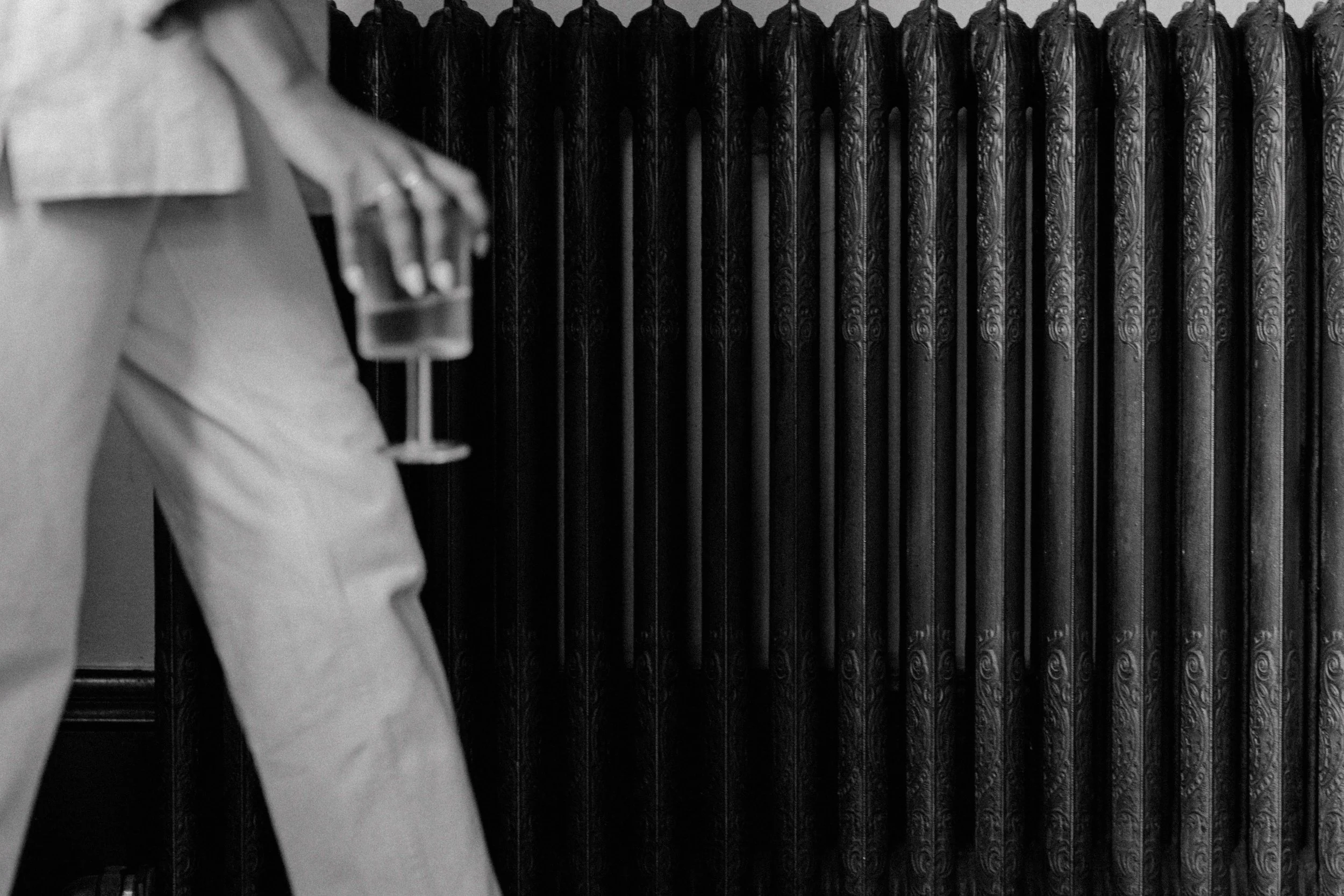 A person wearing a suit and glasses holding a small display case with a ring, standing next to an ornate, carved black radiator.Katie McFarlan Dakota Design Company Best Client Process Templates for Interior Designers