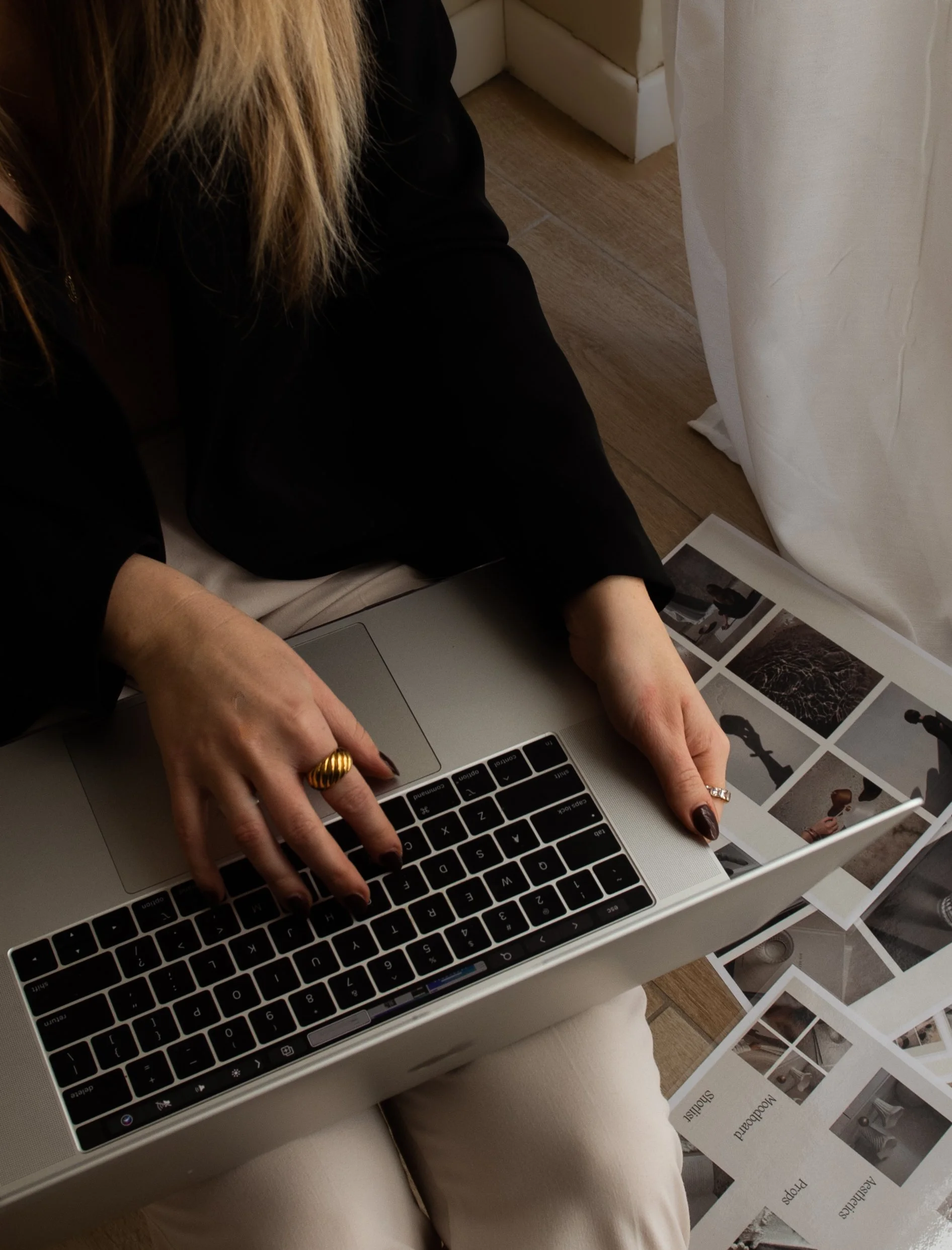 A person with blonde hair, wearing a black top and gold jewelry, sitting on a beige cushion.Katie McFarlan Dakota Design Company Best Client Process Templates for Interior Designers