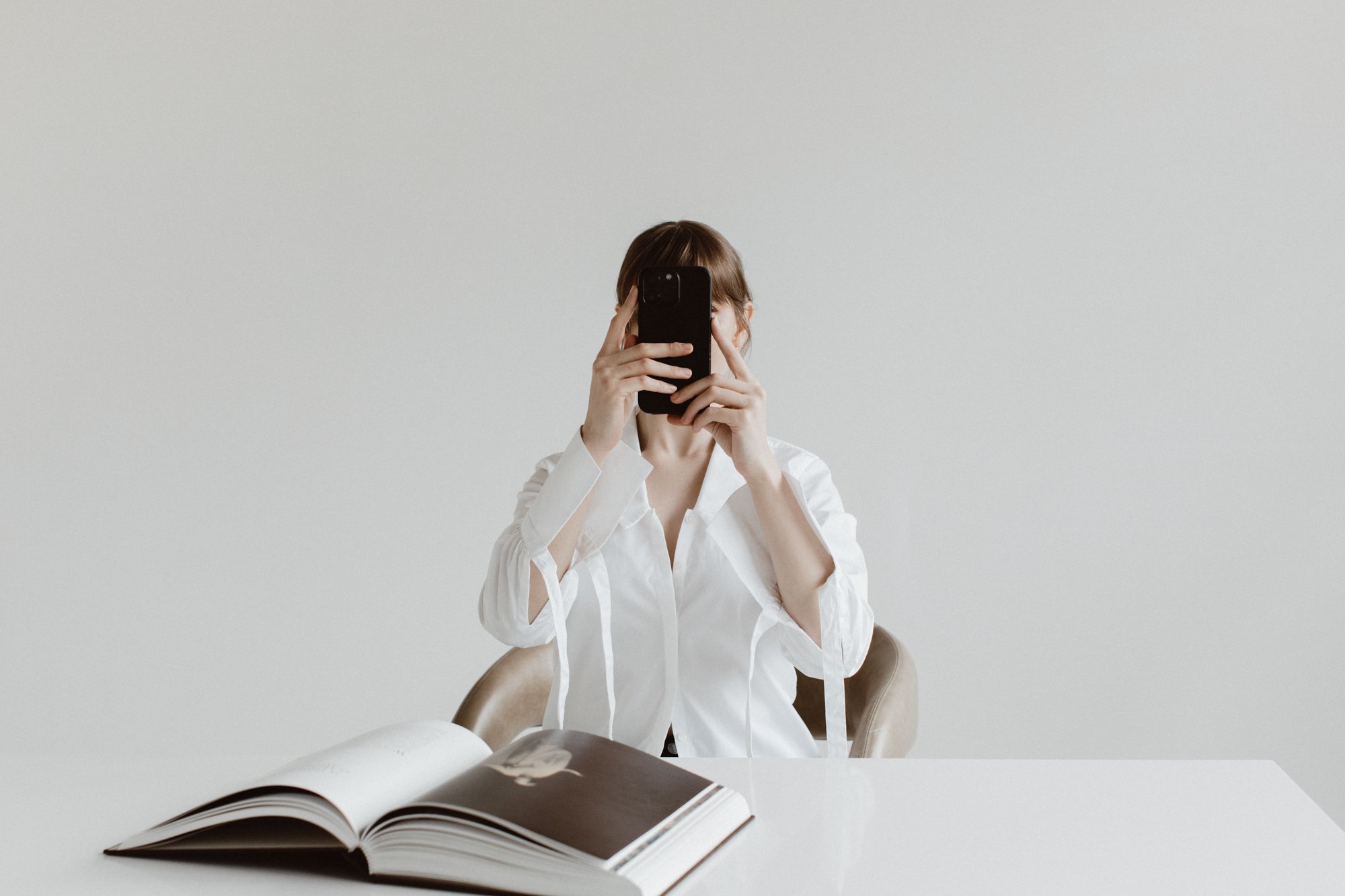 Woman sitting at a desk holding a phone in front of her face.Katie McFarlan Dakota Design Company Best Client Process Templates for Interior Designers