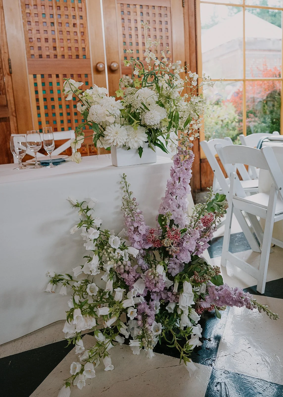 A closeup of modern, whimsical reception flowers arranged around the sweetheart table. The ground arrangement is amde of white campanula, purple delphinium and milkweed.