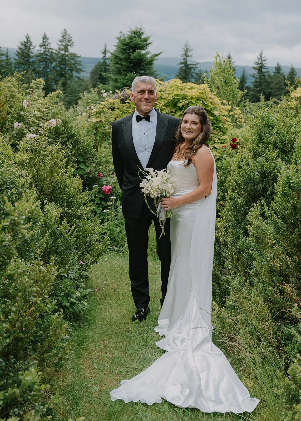A bride stand next to her father holding a modern white calla lily bouquet