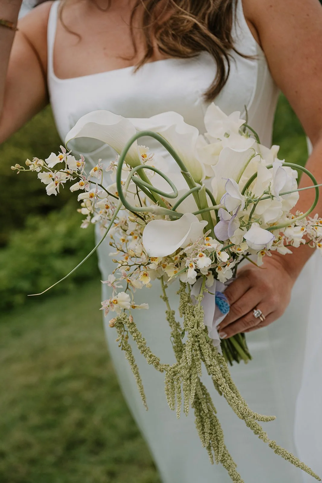 A modern bridal bouquet that is sculptural and embraces color blocking. Flowers include  green garlic scapes, cream oncidium orchids, purple and white sweet pea, and white calla lilies