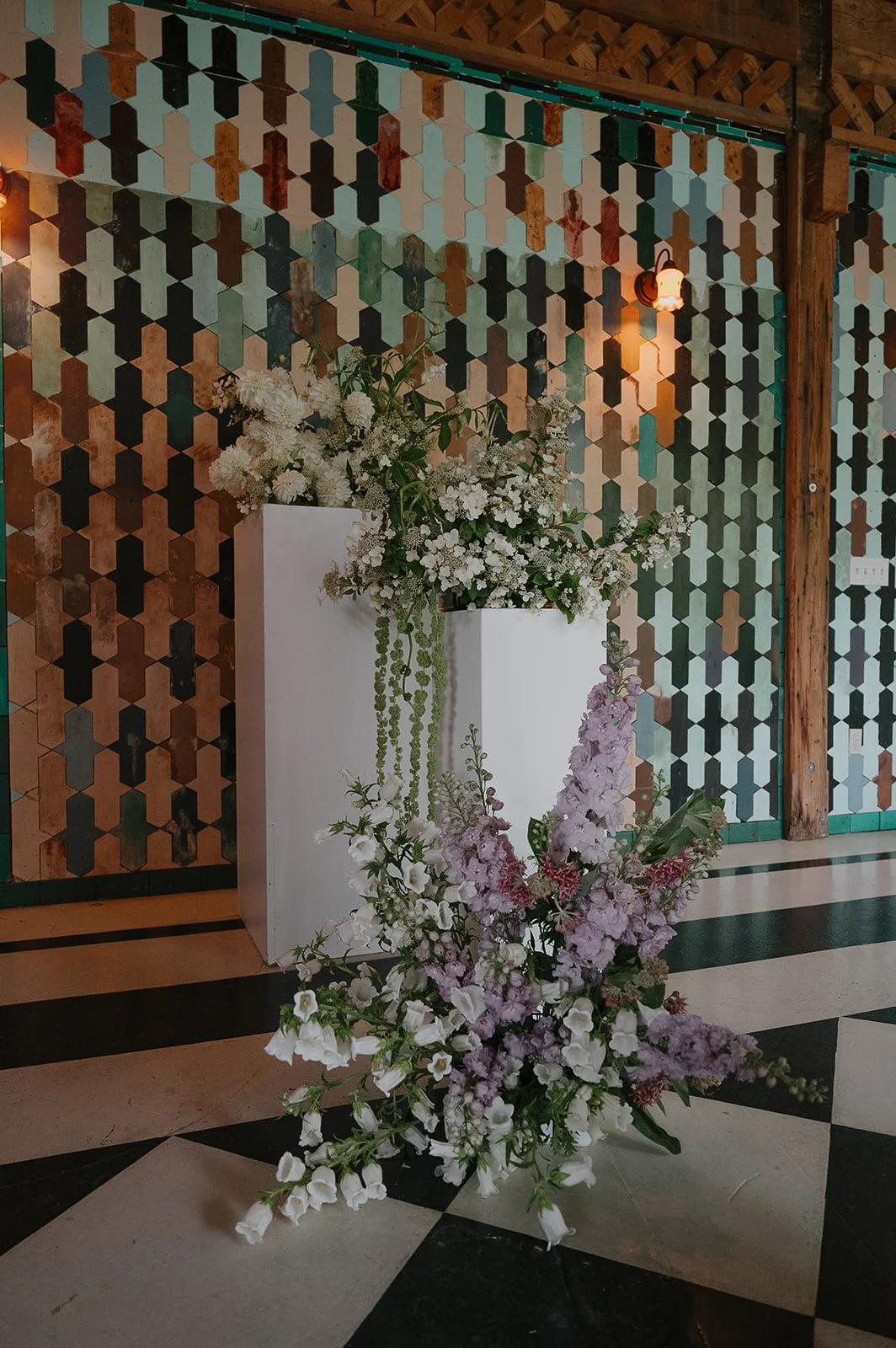 A closeup of one side of a wedding ceremony flower installation. Modern, color-blocked pastel flower arrangements sit atop 2 white pillars and on the ground in front.