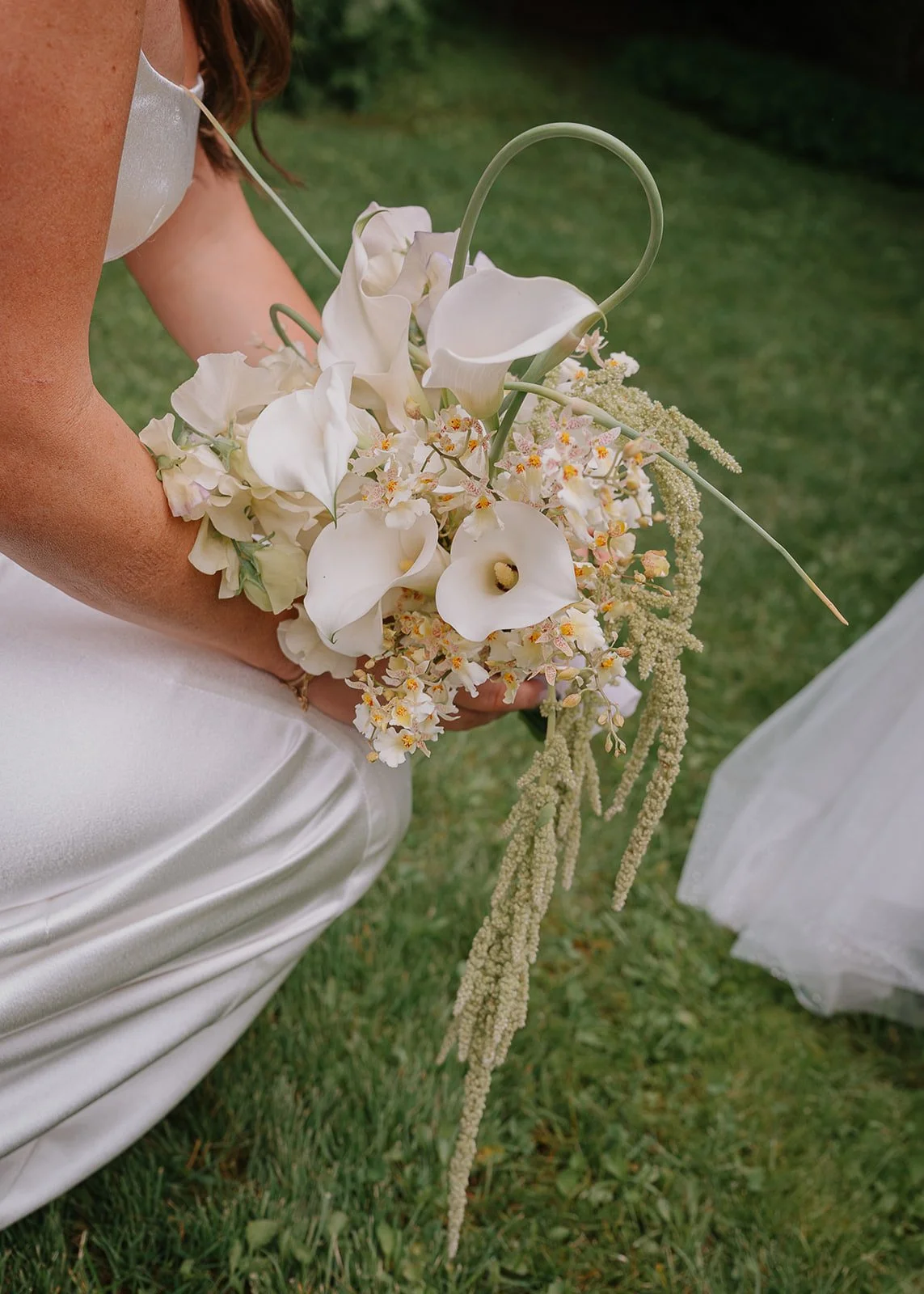 A close up of a bride holding a unique bridal bouquet of calla lilies, orchids, scapes, sweet pea and amaranth
