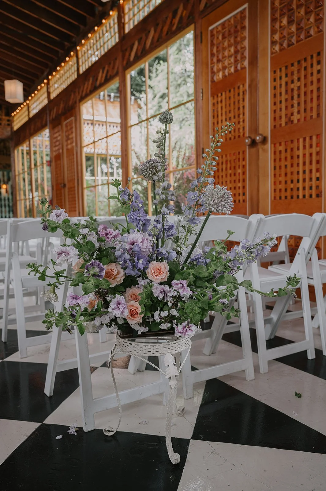 A closeup of a garden-inspired, modern aisle arrangement placed at the entrance of the aisle. Flowers include petunias, allium, roses, delphinium and geranium