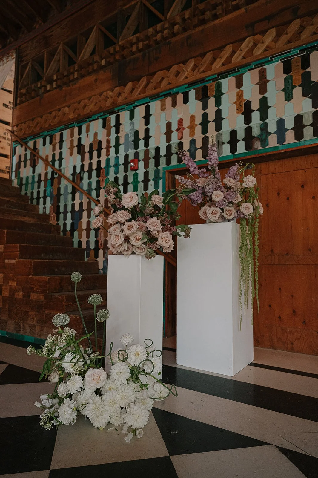 A closeup of one side of a wedding ceremony flower installation. 2 white pillars with flower arrangements on top and one ground arrangement.