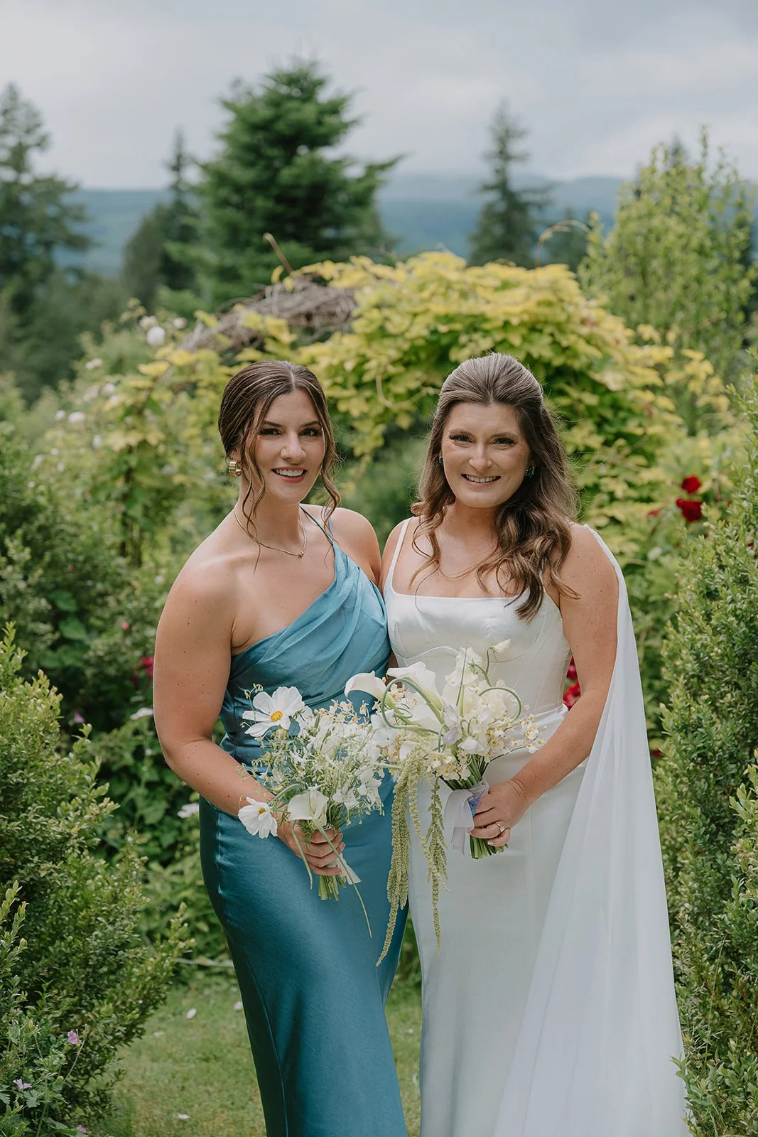 A Bride and bridesmaid stand together holding stunning white bouquets.