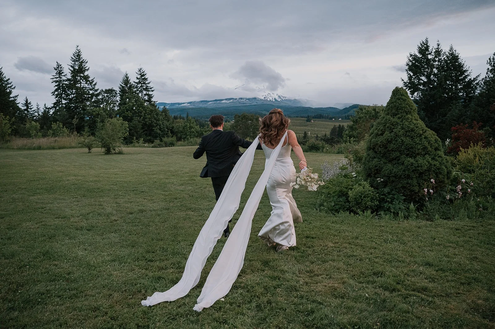 A brida and groom running through the fields of Mt. Hood Organic Farms with sweeping views of Mt. Hood
