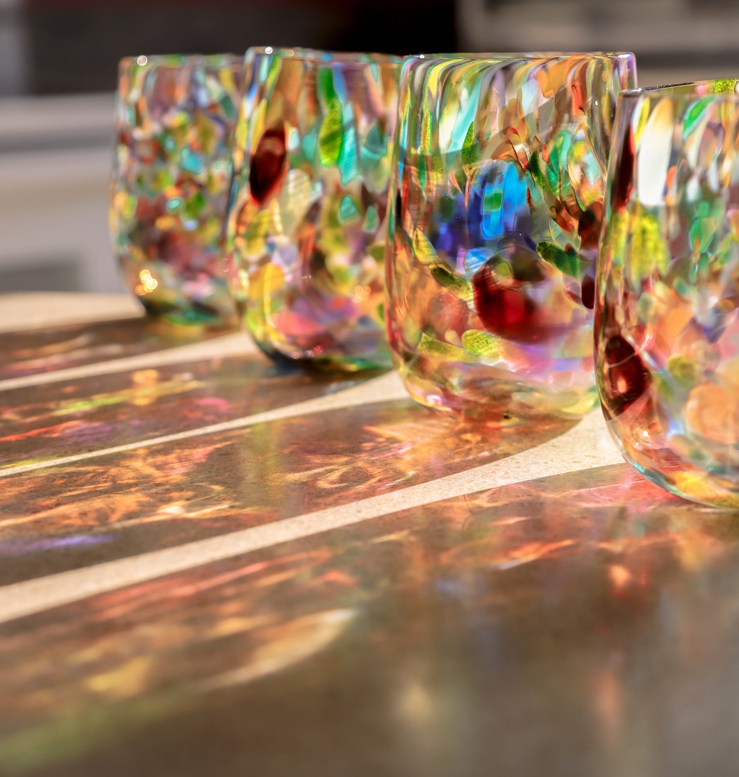 4 bllown glass stemless wine glasses - speckled with many colours - with sun shining through the cups with a reflection on the counter