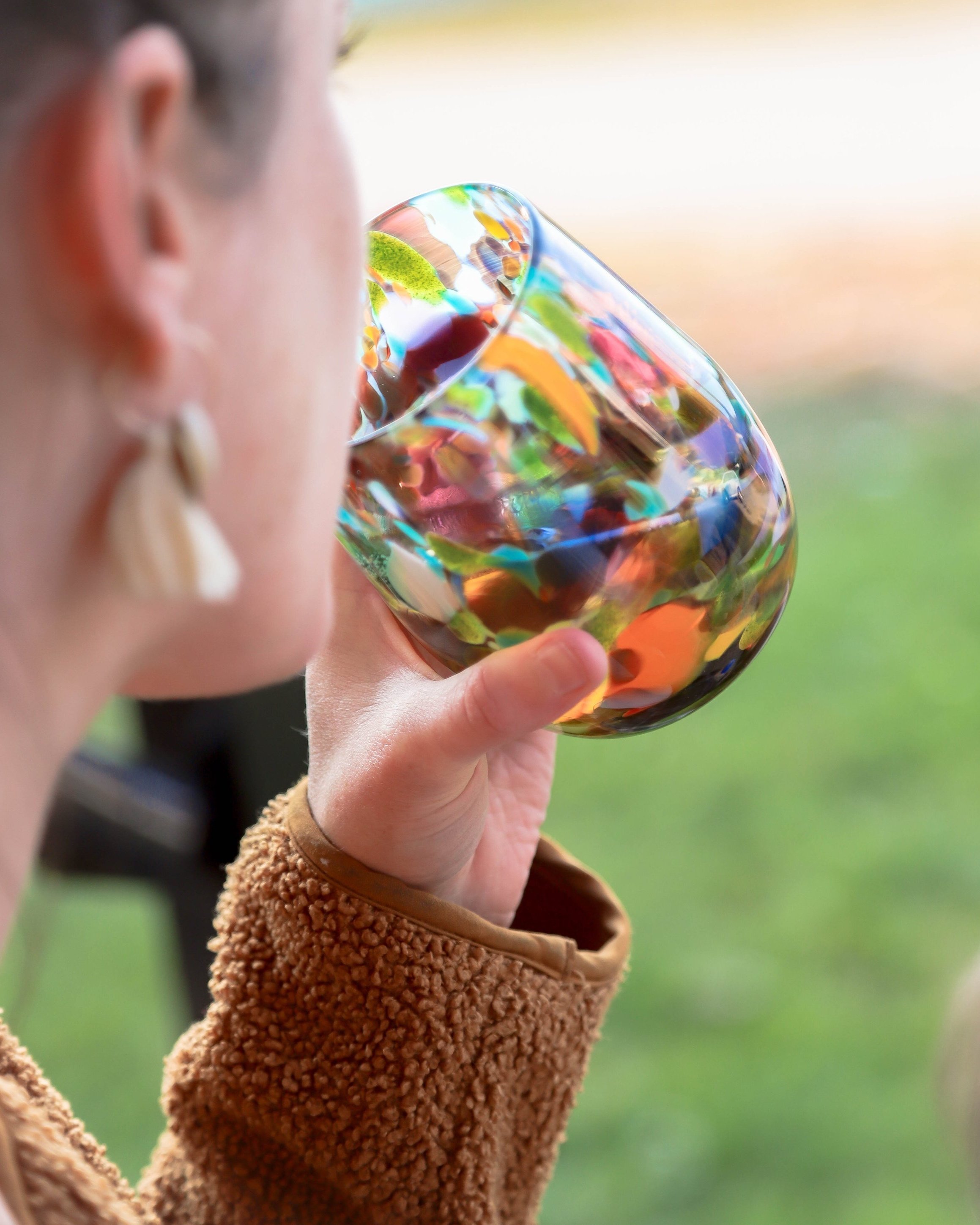 Woman drinking out of a blown glass stemless wine glass - speckled with many colours