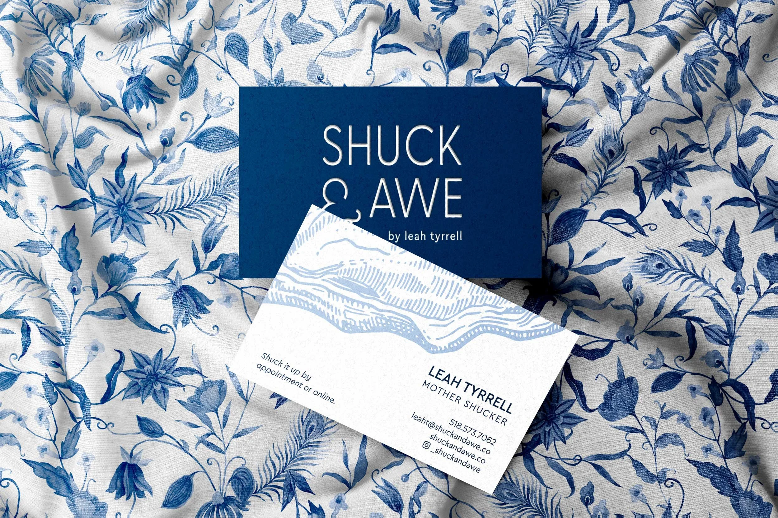 Business card for 'Shuck & Awe,' with a blue and white floral background, contact info including email, phone, website, and social media handle.
