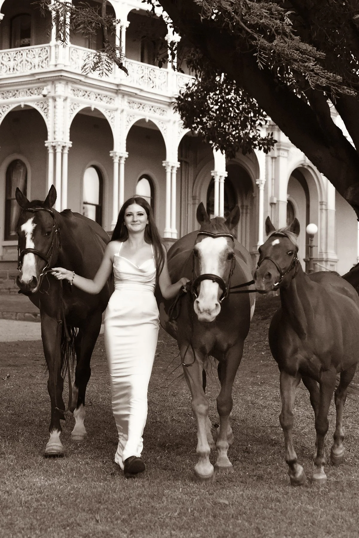 Young woman in a white dress leading three horses outside historic mansion in Sunbury, Victoria - fine art equestrian photogtraphy.