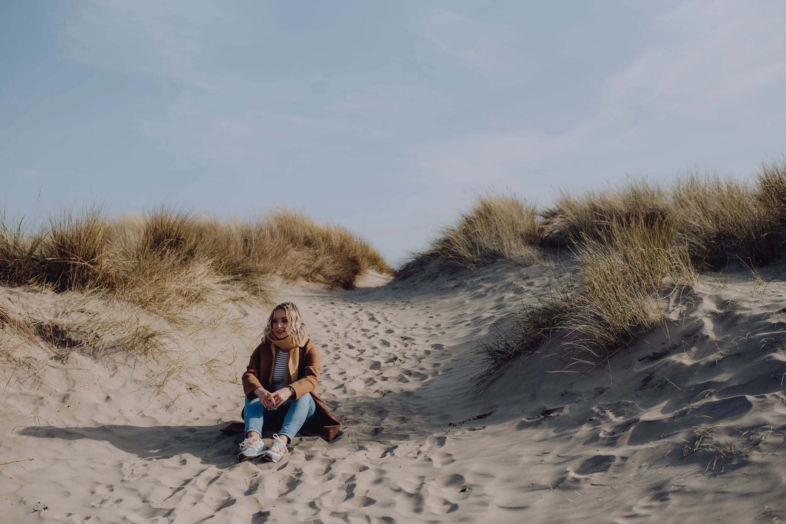 Mari sitting on the sand between sand dunes with grass on a beach