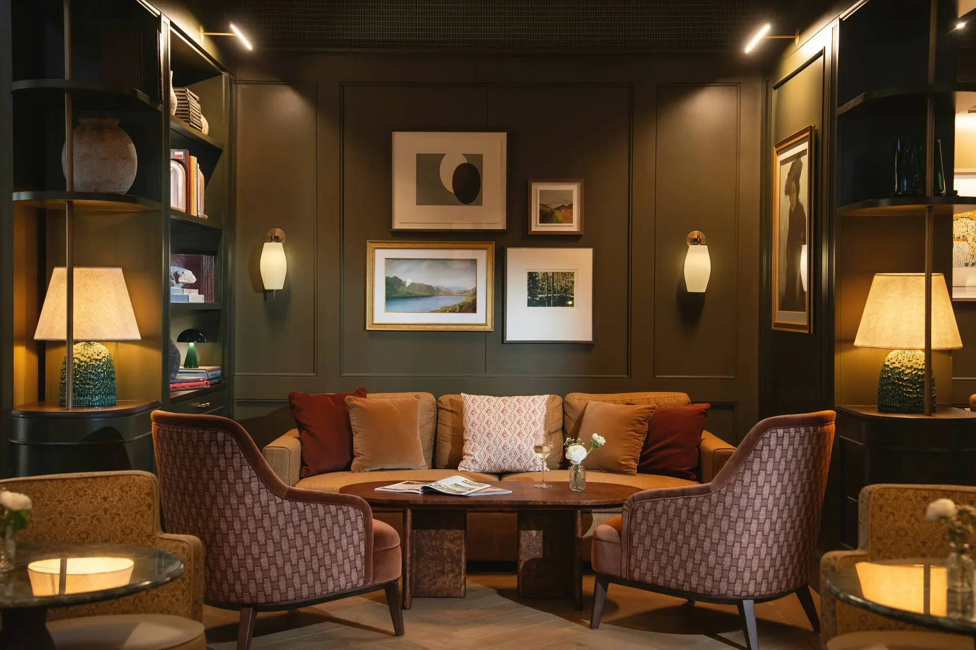 The Grace, Westport Estate, warmly lit lounge with a sofa, patterned armchairs, round coffee table, built-in bookshelves, lamps, and framed artwork.