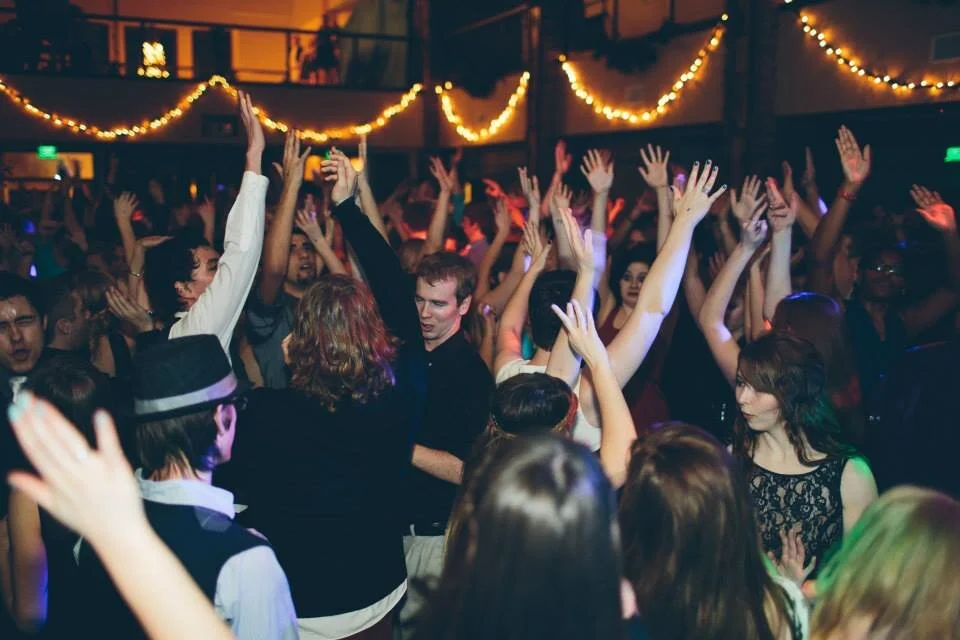People dancing and having fun at a party or nightclub with string lights overhead.