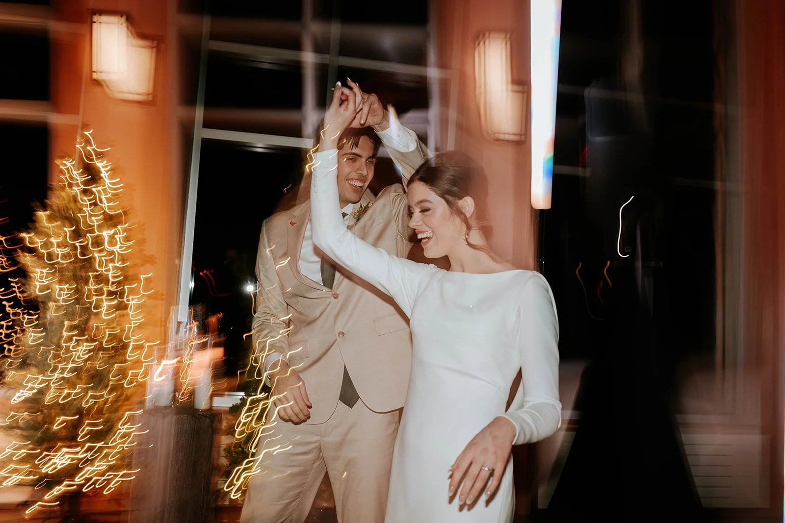 A bride and groom dancing at their wedding reception with blurred lighting and decorations in the background.