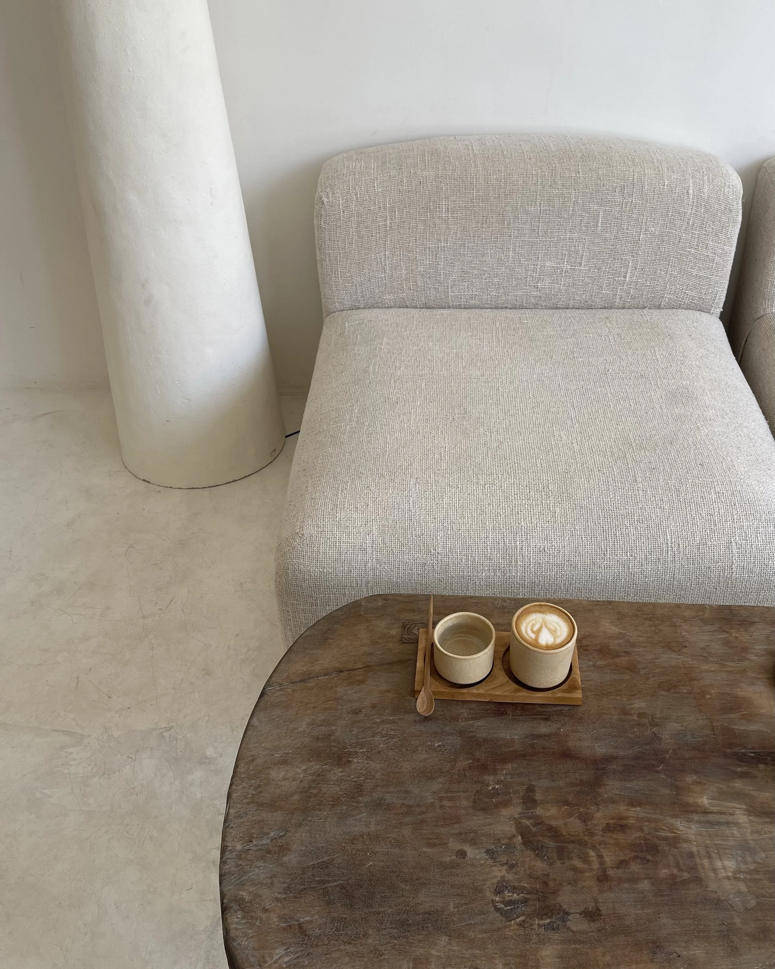 Kahvi ja tee aseteltu puiselle alustalle pöydällä, taustalla beige sohva ja valkoinen seinä.