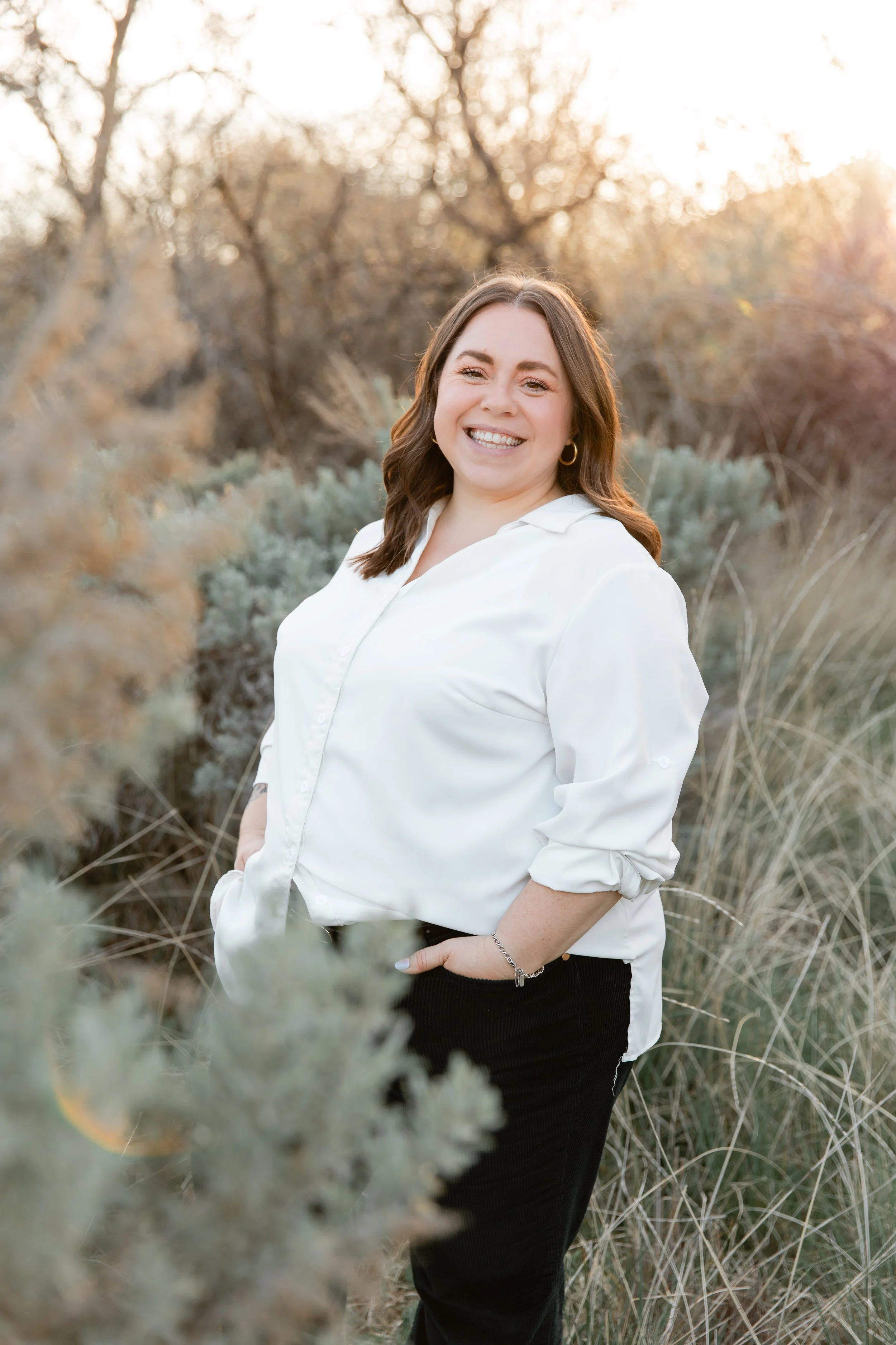 Women in a white shirt and green pants stands outside and is smiling.