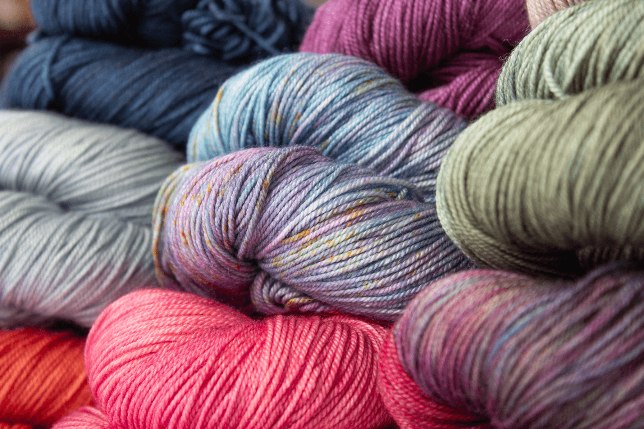 A close-up view of many skeins of yarn in various colors including pink, blue, purple, gray, and green.