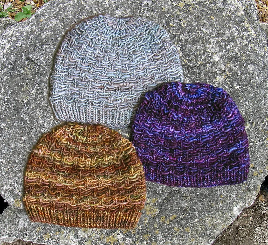 Three colorful knitted hats displayed on a textured stone surface, showcasing their unique patterns and craftsmanship.