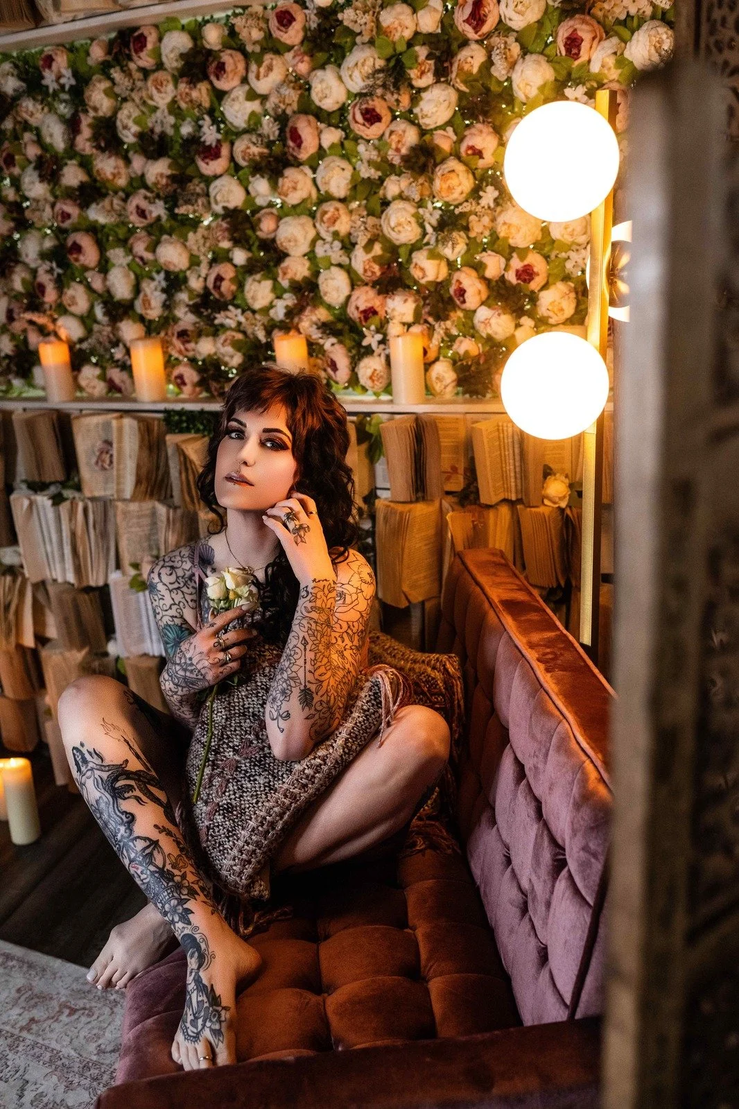 Tattooed woman holding roses on a velvet chair in our private boudoir studio