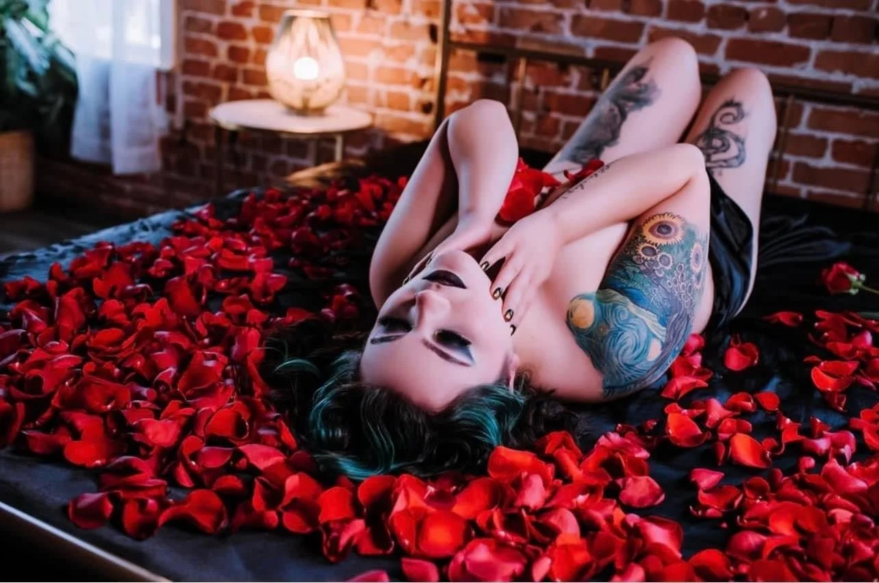 Tattooed woman lying in red rose petals during a boudoir session near Fort Collins