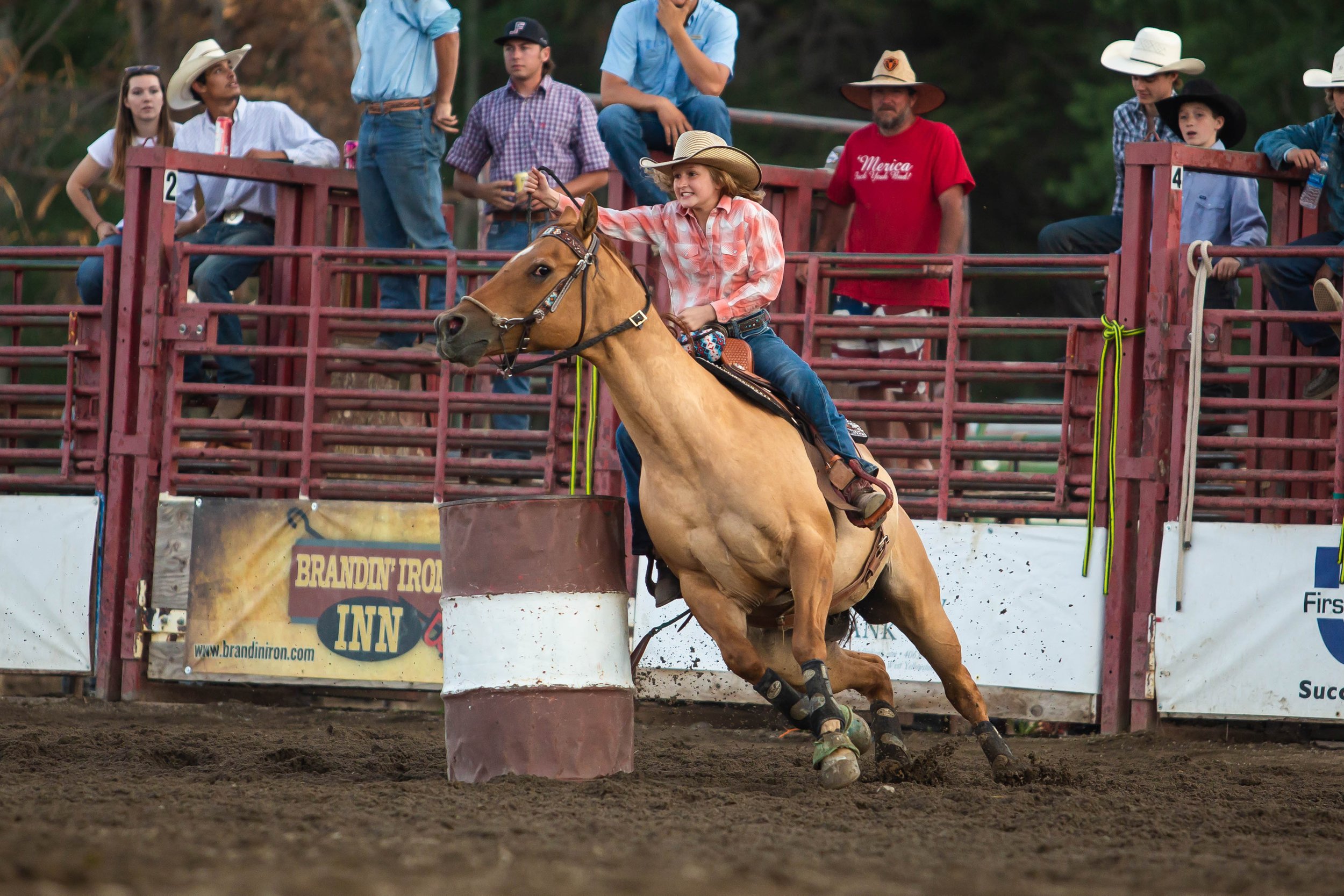 Young girl riding a horse around a barrel during a rodeo event.