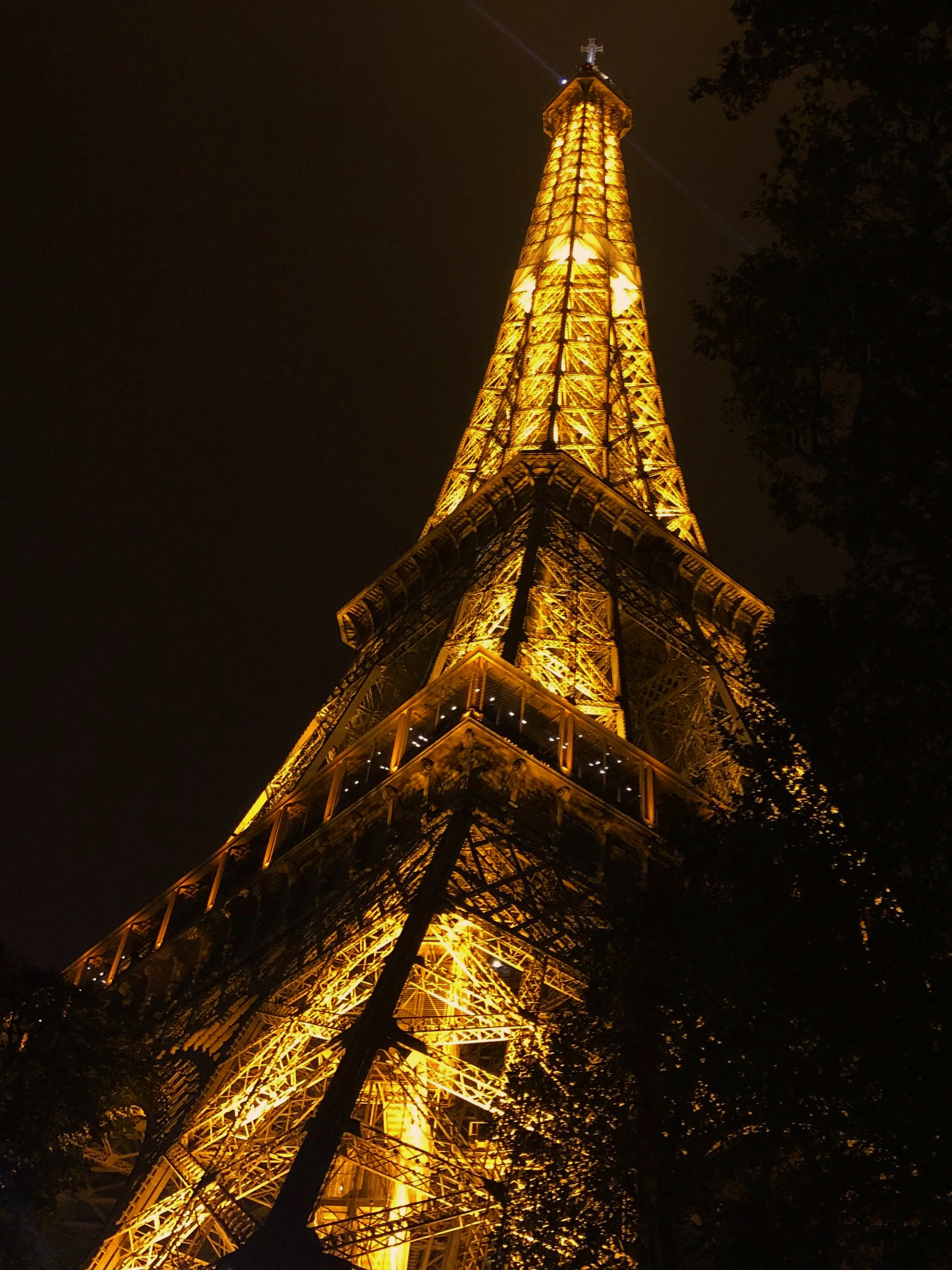 A tall, illuminated Eiffel Tower replica at night surrounded by dark sky and trees.