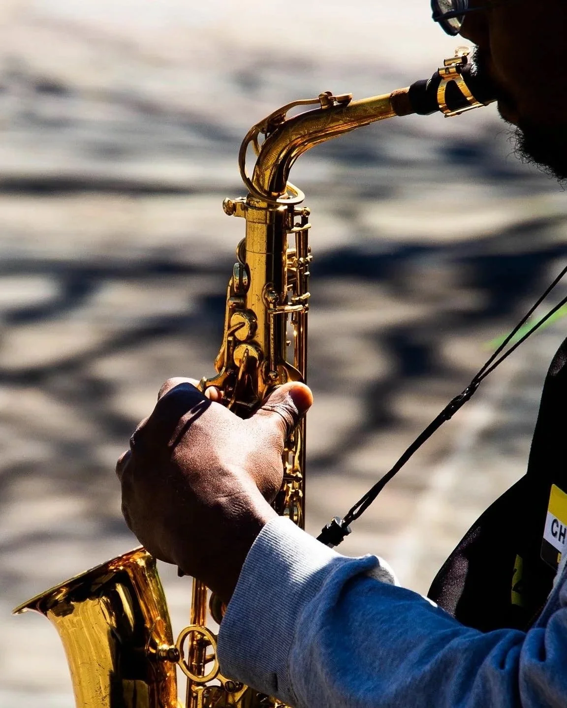 A person playing a gold saxophone near a body of water, possibly during the evening or late afternoon.