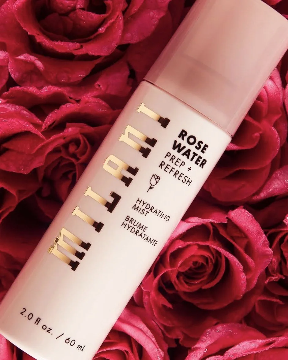 A bottle of hydrating rose water spray placed on a bed of pink roses.
