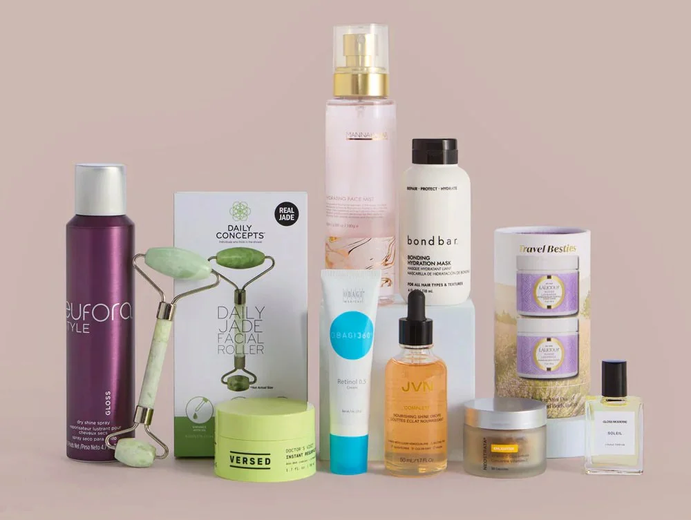 Collection of skincare and beauty products including spray bottles, facial roller, mask, creams, serums, and a perfume, arranged on a flat surface.