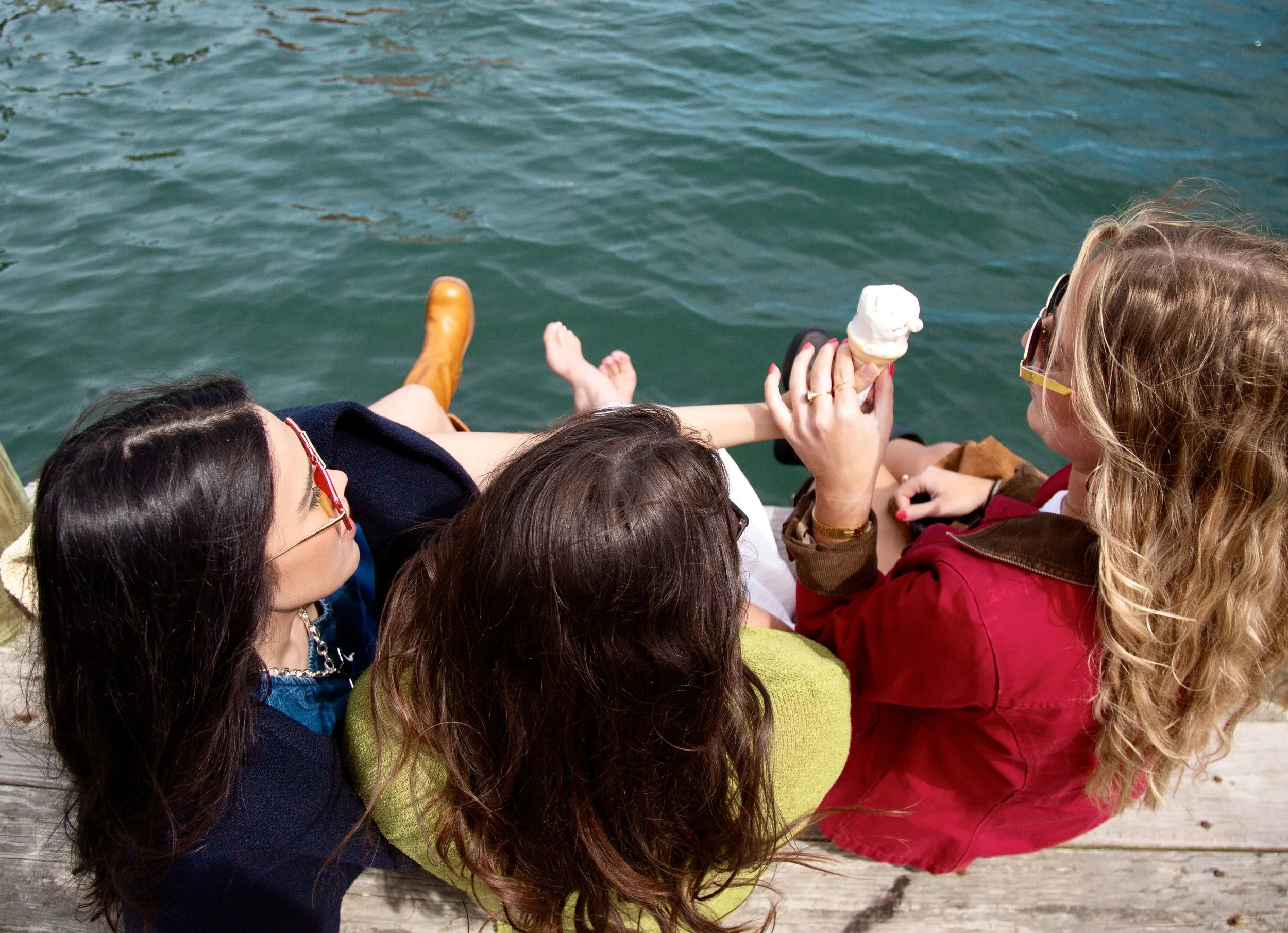 Group of women sitting outdoors by water, one holding an ice cream cone